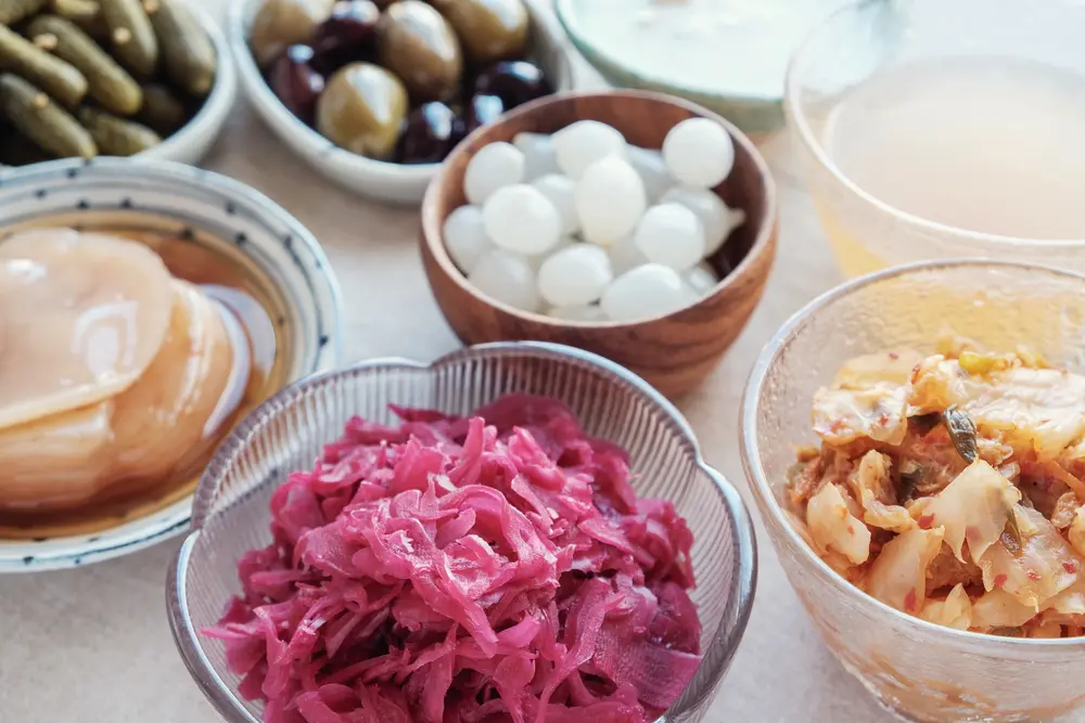 Miski z kiszoną kapustą, kimchi, jogurtem, oliwkami i innymi fermentowanymi produktami.