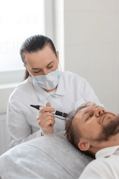 Specjalistka w Turkus Hair Transplant Clinic wykonuje zabieg na linii włosów pacjenta podczas przeszczepu włosów.